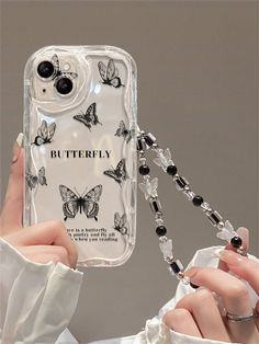 a woman holding up a phone case with butterflies on the back and chain attached to it