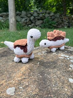 two crocheted stuffed animals sitting on top of a rock next to each other