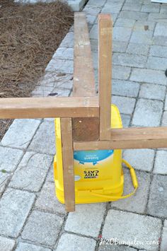 a yellow bucket sitting on top of a wooden bench next to a brick walkway and fence