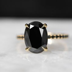 a black diamond ring sitting on top of a white surface with gold trimmings