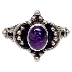 Sterling silver amethyst cabochon ring. Size 7 1/2 Oval bezel set amethyst cabochon in a bright purple color is surrounded by silver bead accents on a black oxidized background. Measures approx 5/8" high at front, center stone measures approx 7.5mm x 5.5mm. Weighs approx 4.5g, 2.9dwt Marked 925 Very nice condition with light tarnish and slight surface scratching. Will come packaged in a gift box or pouch (when possible) and will be shipped US Priority Mail with insurance. CL021324/17KCS Cabochon Ring, Bright Purple, Silver Bead, Ring Size 7, Bezel Setting, Silver Beads, Purple Color, Priority Mail, Fashion Rings