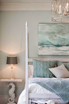 a bedroom with a white bed, blue and green pillows and a painting on the wall