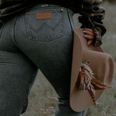 a woman in high waist jeans with feathers on her back, holding a brown bag