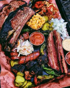 a bbq platter filled with meat, vegetables and condiments on a pink napkin