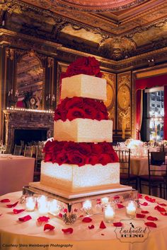 a large wedding cake with red roses on the top is surrounded by candles and flowers