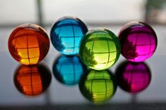 three different colored glass balls sitting on top of a reflective surface with reflections in it