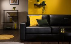 a living room with yellow walls and black leather couches, coffee table and potted plant