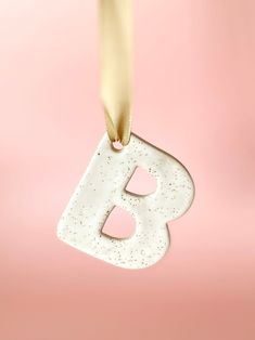 the letter b is hanging from a string on a pink background with gold foiling