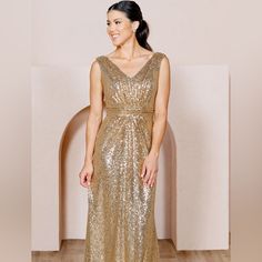 a woman in a gold sequin dress standing on a wooden floor smiling at the camera