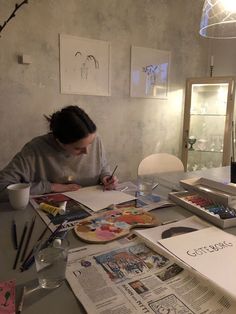 a woman sitting at a table in front of a magazine and watercolors on paper