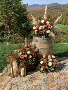 flowers are arranged on the table in front of an old barrel and lantern light with mountains in the background