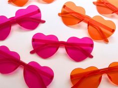 pink and orange heart shaped sunglasses on a white surface with one red pair in the middle