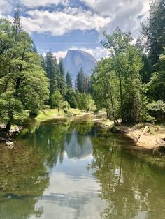 a river surrounded by trees and mountains under a blue sky with white clouds in the background