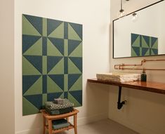 a bathroom with green and blue tiles on the wall next to a wooden stool in front of a mirror