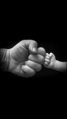 a black and white photo of a baby's hand holding the finger of an adult