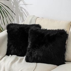 two black furry pillows sitting on top of a couch next to a potted plant