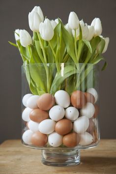 a glass vase filled with eggs and tulips