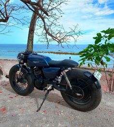 a motorcycle parked on the beach next to a tree