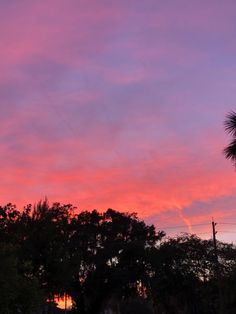 the sky is pink and purple as the sun sets in the distance with palm trees