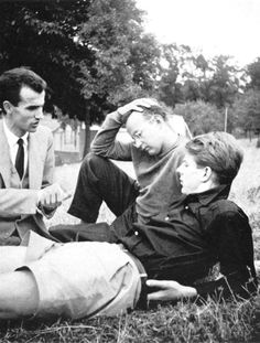 three people sitting on the ground in front of trees and one person holding his head