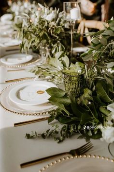 the table is set with white plates and greenery