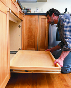 a man kneeling down in front of an open drawer on the kitchen floor, looking inside