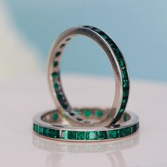 two wedding bands with emerald colored stones on them