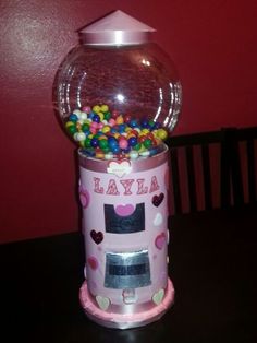 a gummy machine with lots of candy in it on a table next to a red wall