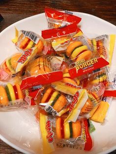 a white plate topped with lots of hot dogs and hamburger wrapped in plastic wrappers