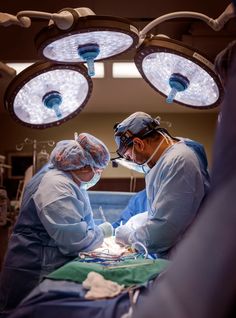 two surgeons performing surgery on a patient in an operating room with three lights above them