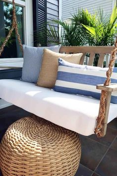 a white porch swing with blue and white pillows sitting on it's back end