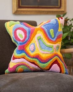 a colorful pillow sitting on top of a couch next to a plant in a living room