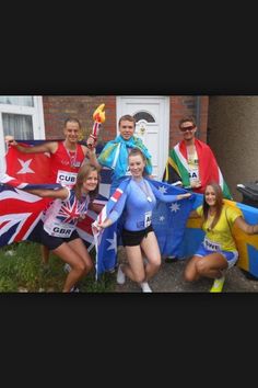 a group of people standing next to each other in front of a house holding flags