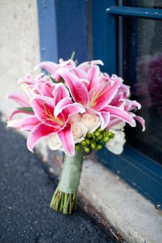 a bouquet of pink lilies and white roses sits in front of a blue window