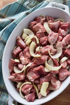 meat and onions in a white bowl on a wooden table next to a blue towel