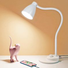 a pink cat figurine next to a white lamp on a table with a cell phone