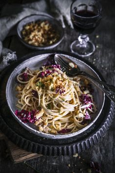 a plate of pasta with red cabbage and parmesan cheese next to a glass of wine