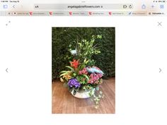 a vase filled with lots of flowers on top of a wooden table next to a computer screen