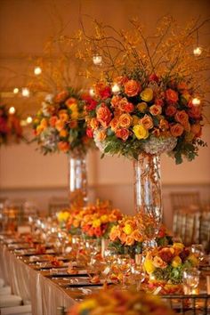 an arrangement of flowers in vases on a long table with candles and place settings