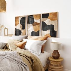 a bed with pillows and blankets on top of it next to two framed art pieces