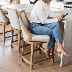 a woman sitting at a kitchen counter using her cell phone while holding a smart phone