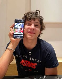 a young man holding up his cell phone to take a selfie in front of him