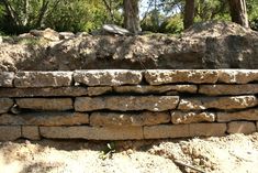 a pile of rocks sitting on top of a dirt ground next to trees and bushes