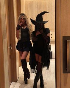 two women dressed up as witches in a hallway with doors open and one wearing a black dress