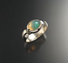 "This is a very bright and colorful natural Opal from Ethiopia. Set in a bezel east-west style with a 6mm wide low dome smooth band. The stone is clean and displays mint green and powder blue colors in a crystal base. Stone measures 8x10mm. Specify your ring size in a \"note to seller\" at check out." Modern Oval Cabochon Opal Ring, Modern Green Round Dome Ring, Green Oval Opal Ring With Bezel Setting, Modern Oval Opal Ring With Bezel Setting, Modern Round Opal Ring, Green Domed Jewelry With Polished Finish, Modern Opal Ring With Bezel Setting, Modern Domed Ring With Bezel Setting, Powder Blue Color