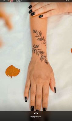 a woman's hand with black nail polish and leaves on her left arm, next to an orange leaf