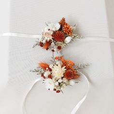 two bridal bouquets with orange and white flowers are tied to a white ribbon