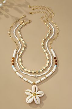 a necklace with white beads and flowers on the front, hanging from a gold plated chain