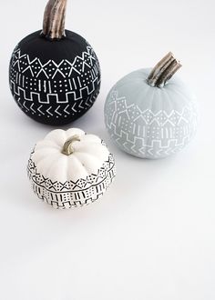 three painted pumpkins sitting next to each other on a white surface with black and white designs