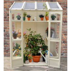 an outdoor greenhouse with potted plants and pots on the side walk in front of a brick wall